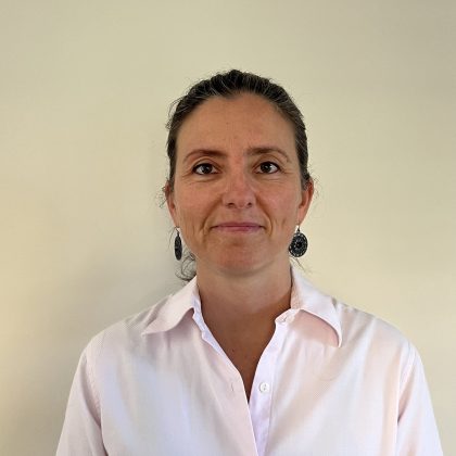 Dr Fiona Beatie smiles at the camera in front of a white wall. She has dark hair pulled back into a ponytail and is wearing a pink shirt