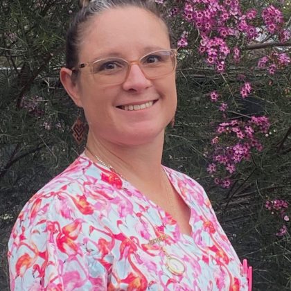 Midwife Michelle Uren smiles at the camera. She is wearing a colourful scrubs top and has glasses.