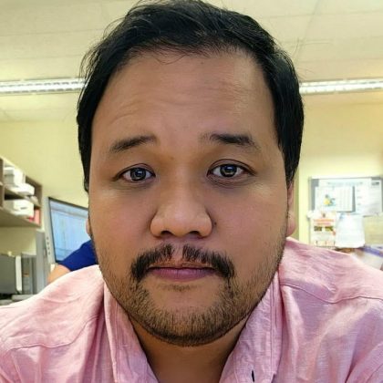 Dr Jordan Cabahug smiles at the camera. He had dark hair and is wearing a pink shirt