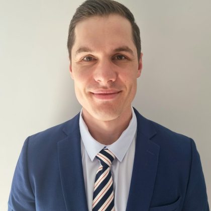 Dr Michael Jashari smiles at the camera. He is wearing a navy suit jacket and a pale blue shirt white a striped tie.
